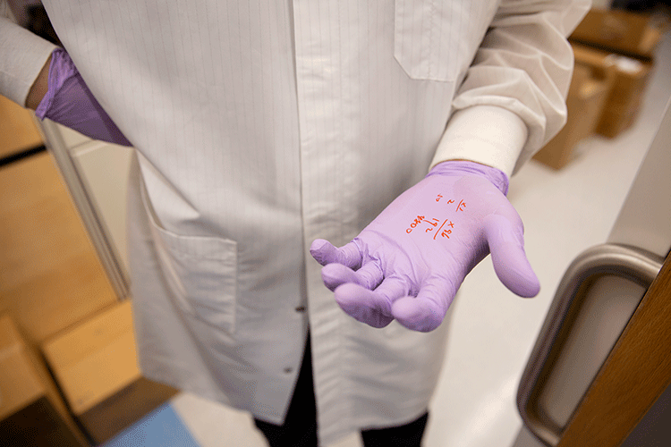 A photo shows a person holding up a gloved hand. Numbers are written on the glove in red pen.