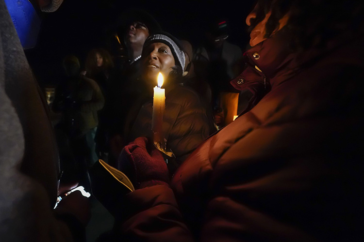 RowVaughn Wells, the mother of Tyre Nichols, a man beaten by Memphis police who died on Jan. 25, 2023, is surrounded by people holding candles in the dark. She is wearing warm clothes.