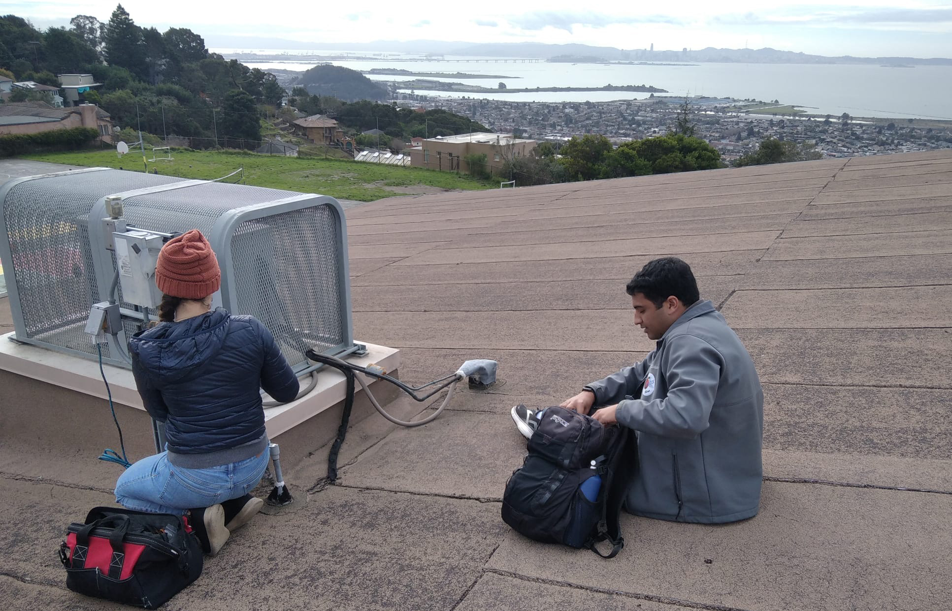 a man and woman on a roof with packs working on equipment with the SF skyline in background