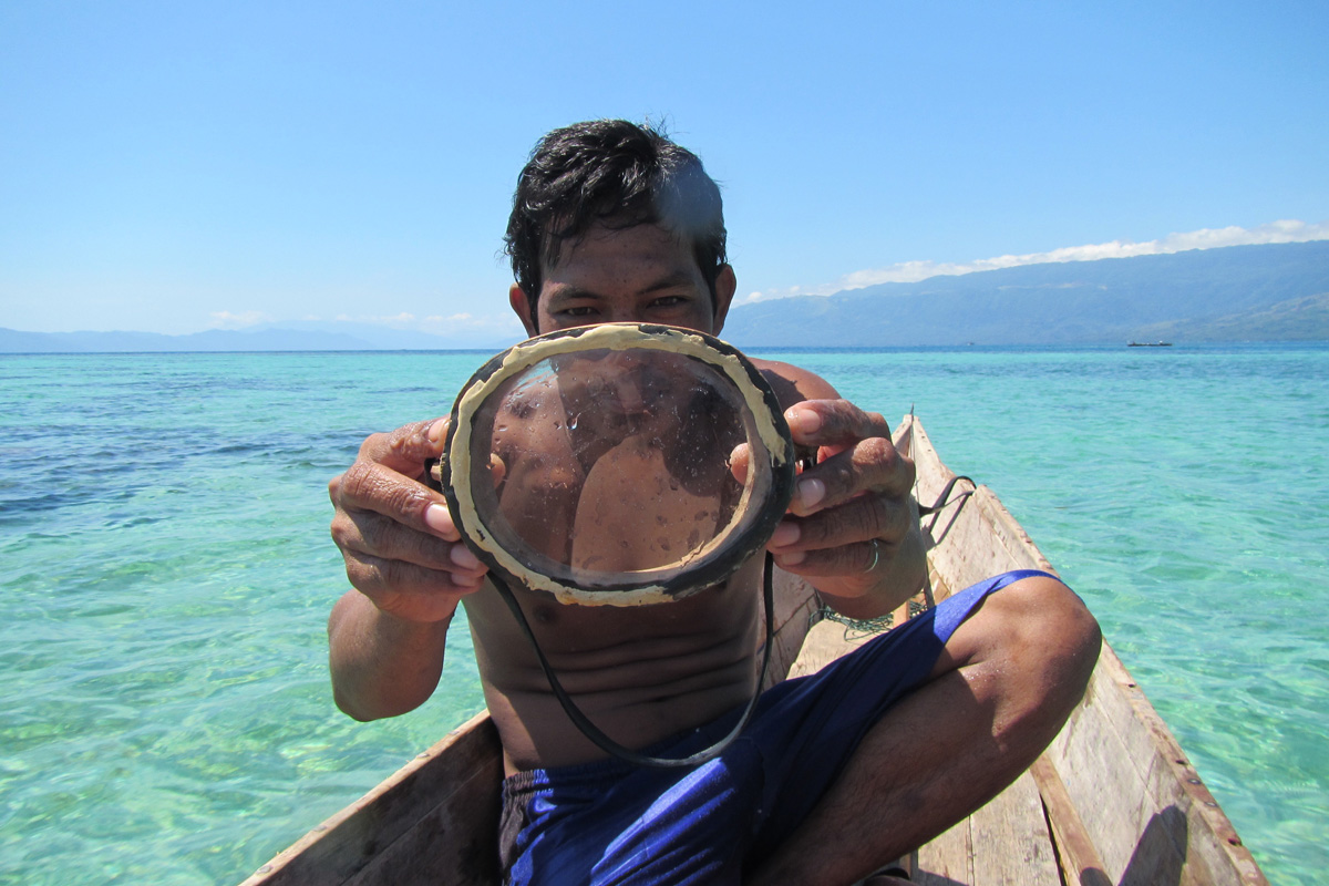 A Bajau diver, sitting in a boat on the water, carrying a mask that he made