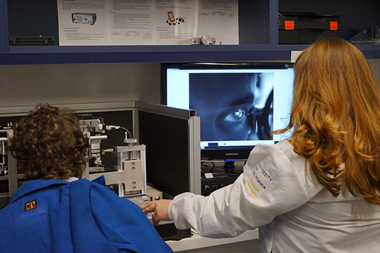 A woman wearing a white lab coat facing a computer scanning a patient's eye.