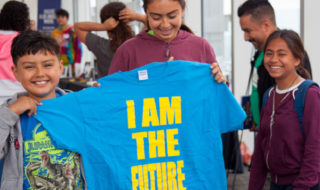 students hold blue shirt that reads "I AM THE FUTURE"