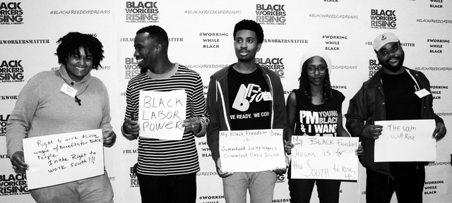 Group of people holding signs in front of Black Workers Rising background