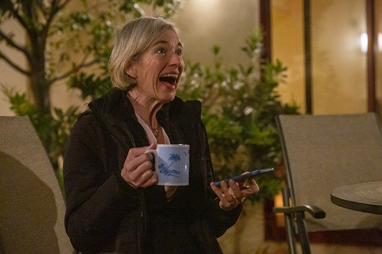 Jennifer Doudna laughs with a cup of coffee in her hand and a phone in the other hand