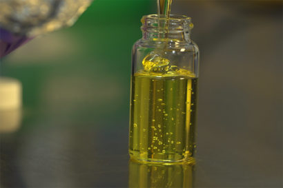 A thick yellow liquid is being poured into a small vial.
