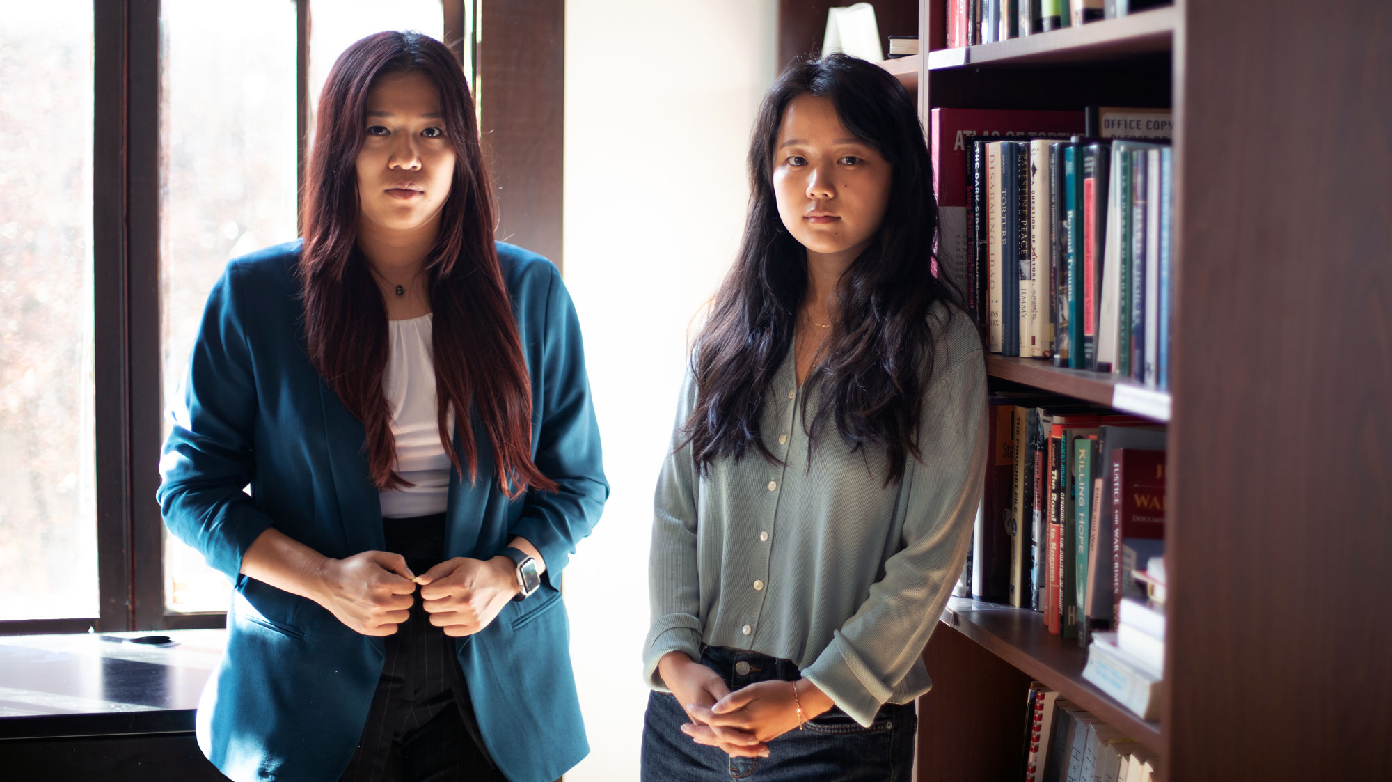 Students Madeleine Wong (left) and Melinda Zou stand in room next to a bookshelf.