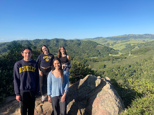 Four students who work with Professor Nicole Starosielski stand together on a large rock with rolling hills in the background