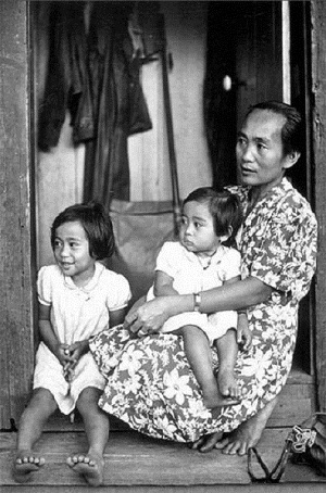 A Filipinx family sits on the stoop of their house looking outdoors.
