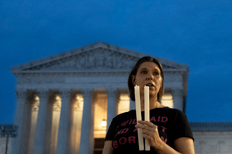 a solemn protester with two candles stands before the US Supreme Court building as darkness falls