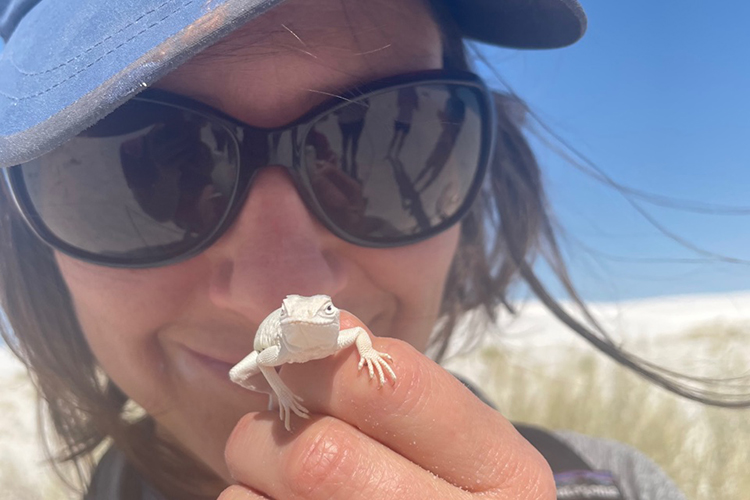 a person wearing a sunglasses holds up a white lizard