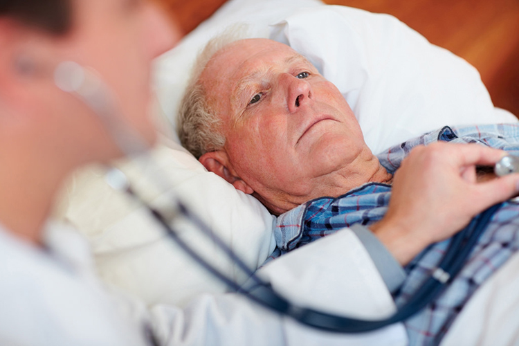 Man lying in bed, doctor using a stethoscope on him