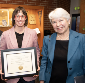Ann Cleaveland holding a framed certificate and Chancellor Carol Christ standing to the right.