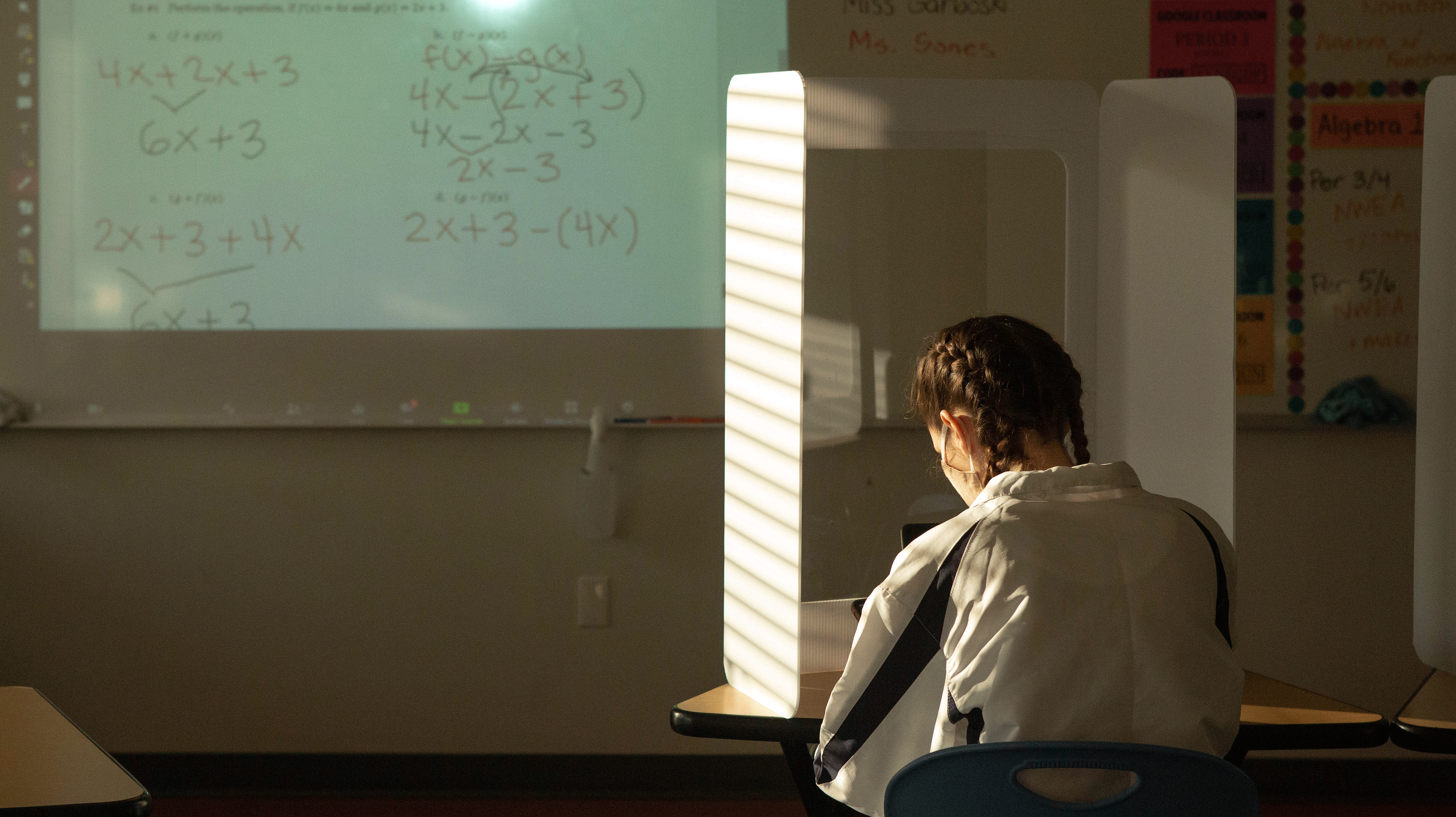 A young woman student in a darkened math class, looking trhough a protective screen at the calculations on a whiteboard