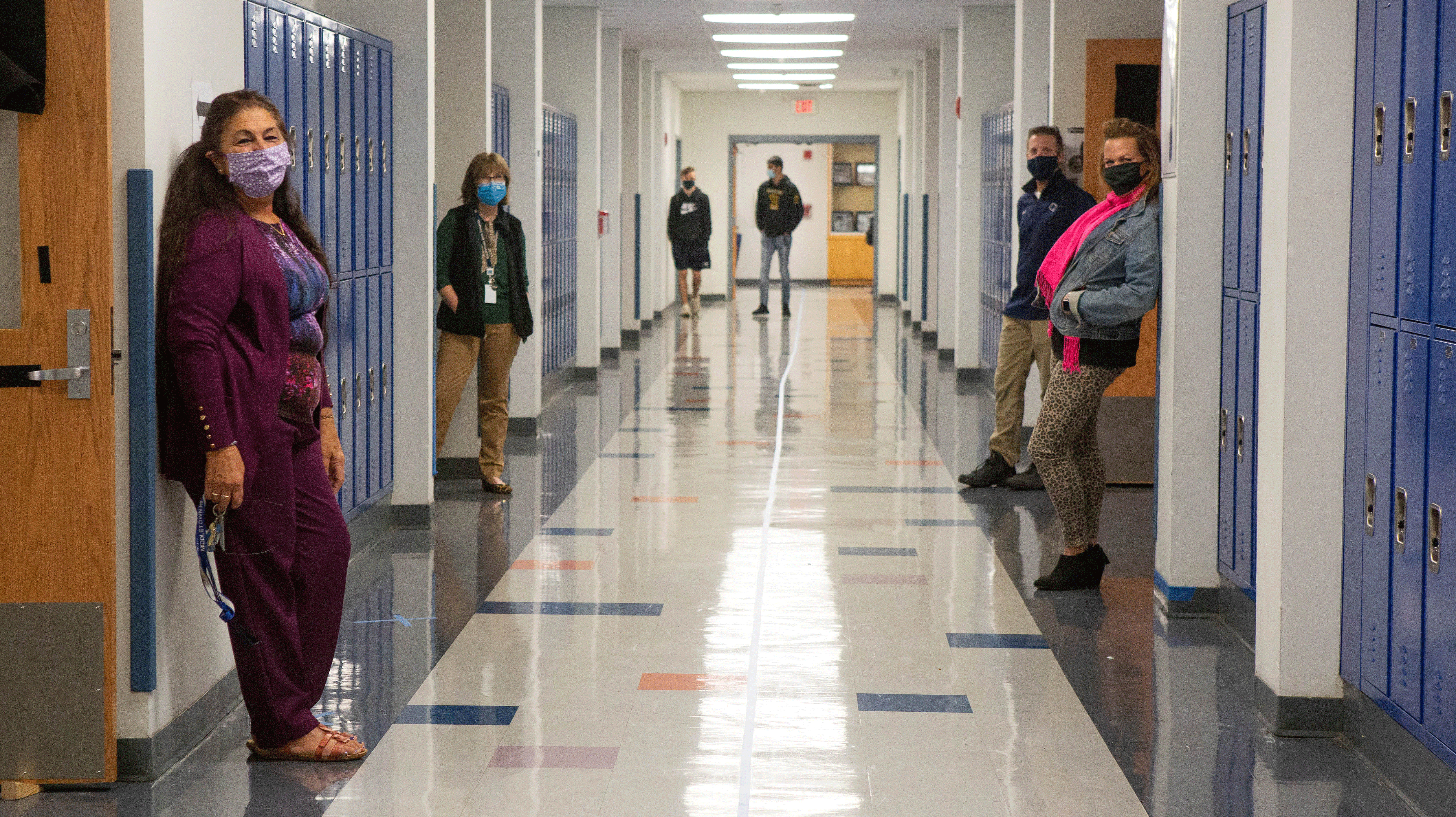 Teachers in a school hallway during the height of the COVID pandemic, wearing masks and socially distanced in a hallway devoid of students