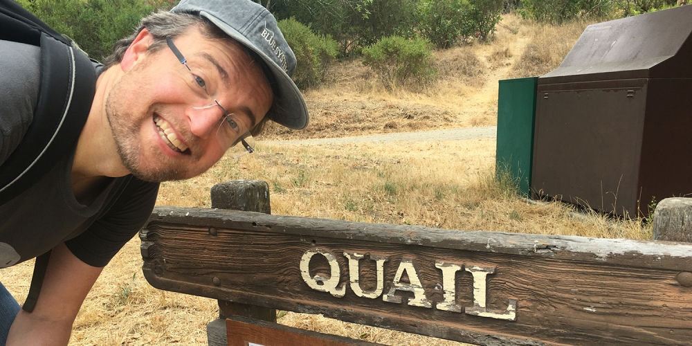 James Quail leaning over a park sign that reads "QUAIL"