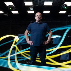 Michael Yartsev standing among light ribbons in yellow and blue.