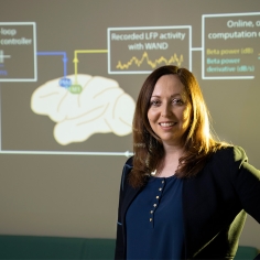 Rikky Muller standing in front of graphic of the brain 