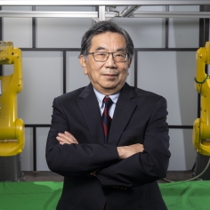 Masayoshi Tomizuka with two industrial robot arms.