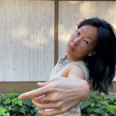 headshot of Asian woman gesturing toward the camera