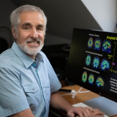 William Jagust sitting in front of a monitor of brain images.