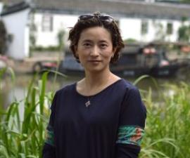 Yue Maria Liu standing outside with greenery in background.