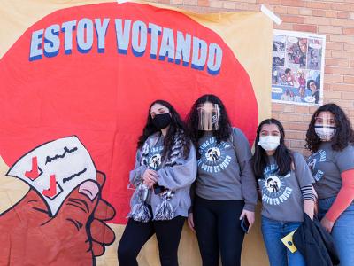 four people pose by a mural that reads "Estoy votando"