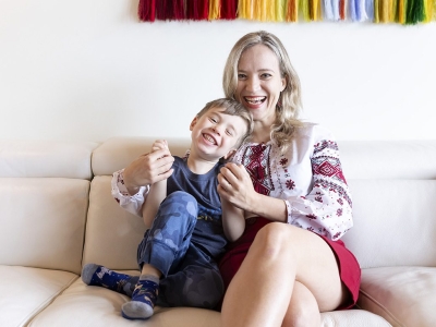 A woman with blond hair sits on a white sofa with her young son. Both are smiling.