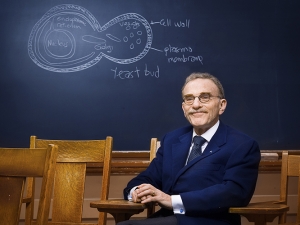 Randy Schekman in blue suit sitting in front of a blackboard