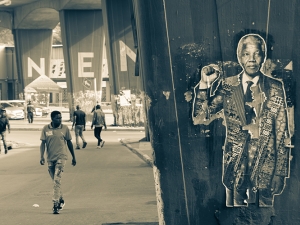 poster of Nelson Mandela on a pillar with people walking along nearby street