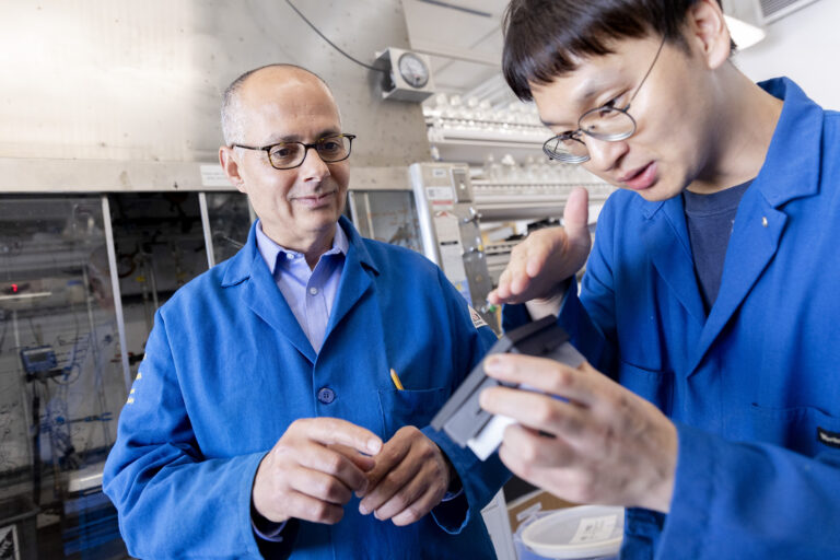 two men in blue coats looking at something in a lab