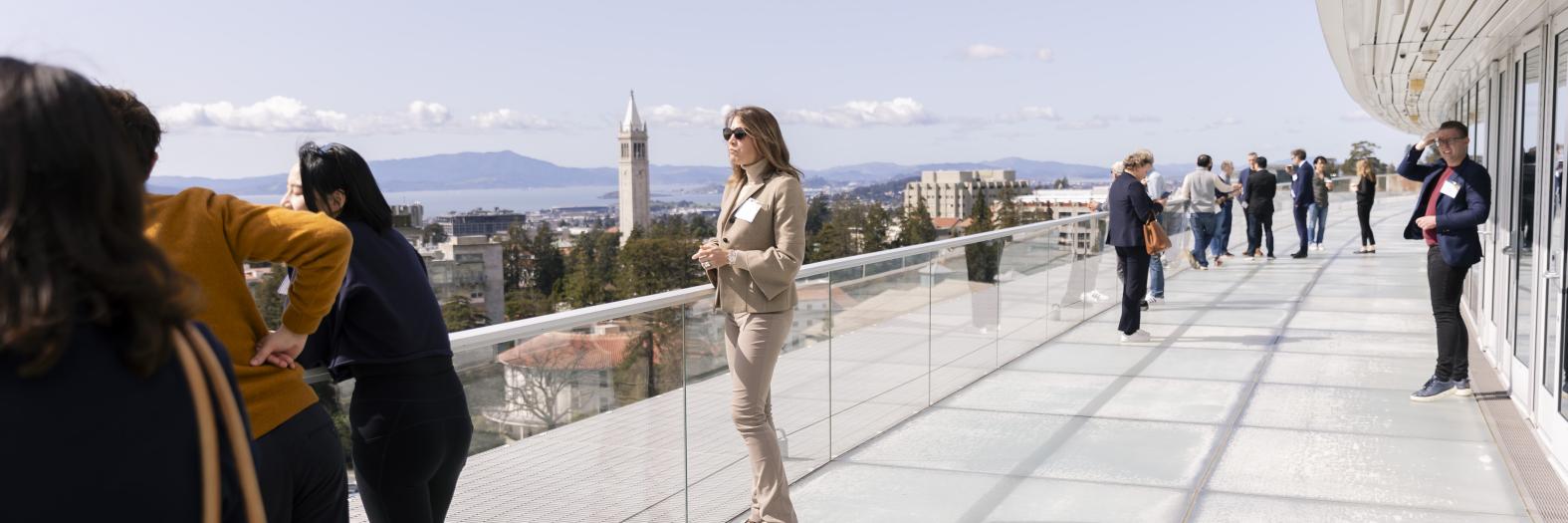 Multiple people standing on outside deck with UC Berkeley campanile and bay in background
