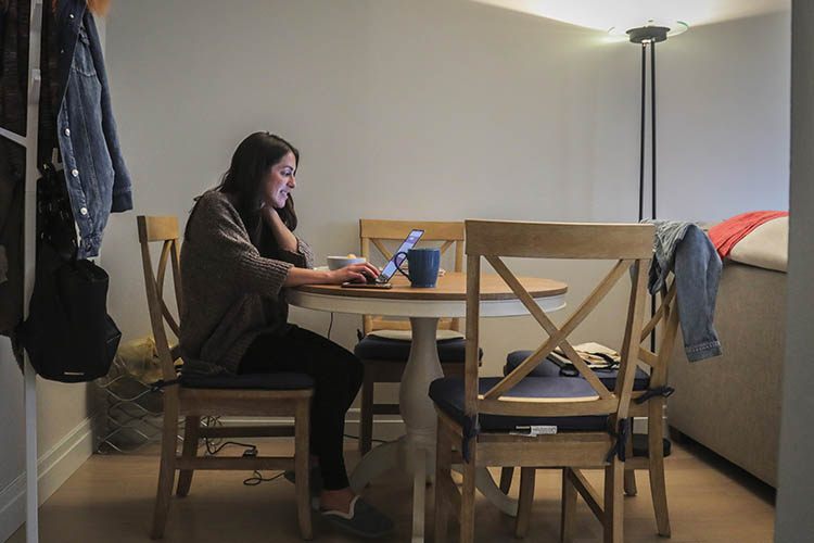 a woman works at a laptop at her apartment dining room table