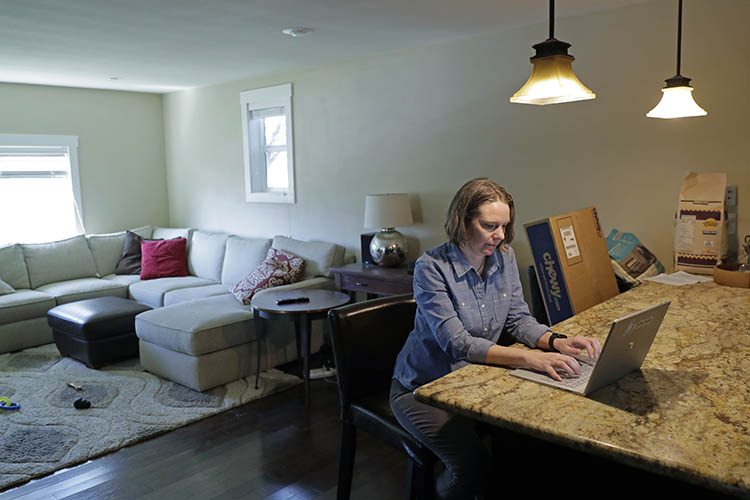 a woman works at a laptop at her kitchen counter