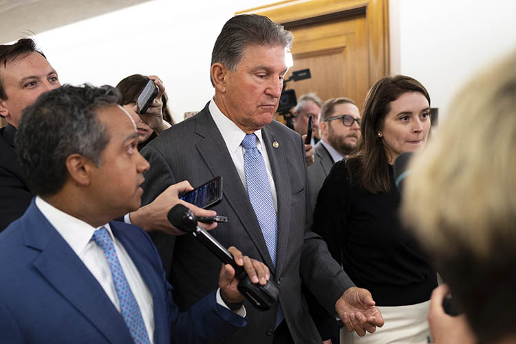 joe manchin talks with reporters while walking down a hallway