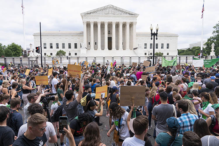 a crowd holding a large mix of abortion-related protest signs stands in front of the supreme court building
