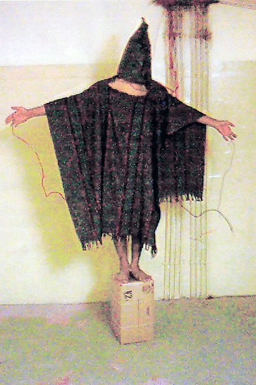 a robed figure with his head covered and wires attached to his fingers—a victim of US torture at the Abu Ghraib prison in Iraq