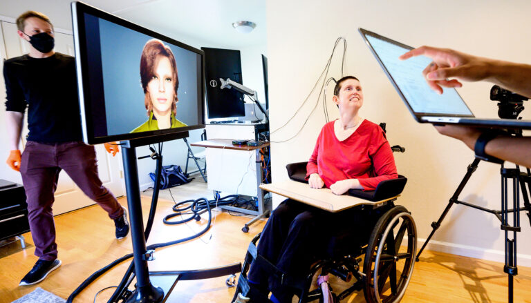 Ann Johnson sits in her wheelchair with a cord plugged into a neuroprosthesis implant while she participates in a clinical trial helping to restore her ability to speak with a brain-computer interface