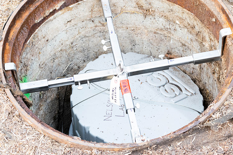 A photo of an autosampler, which looks like a plastic gray trash can, hanging in a sewer hole.