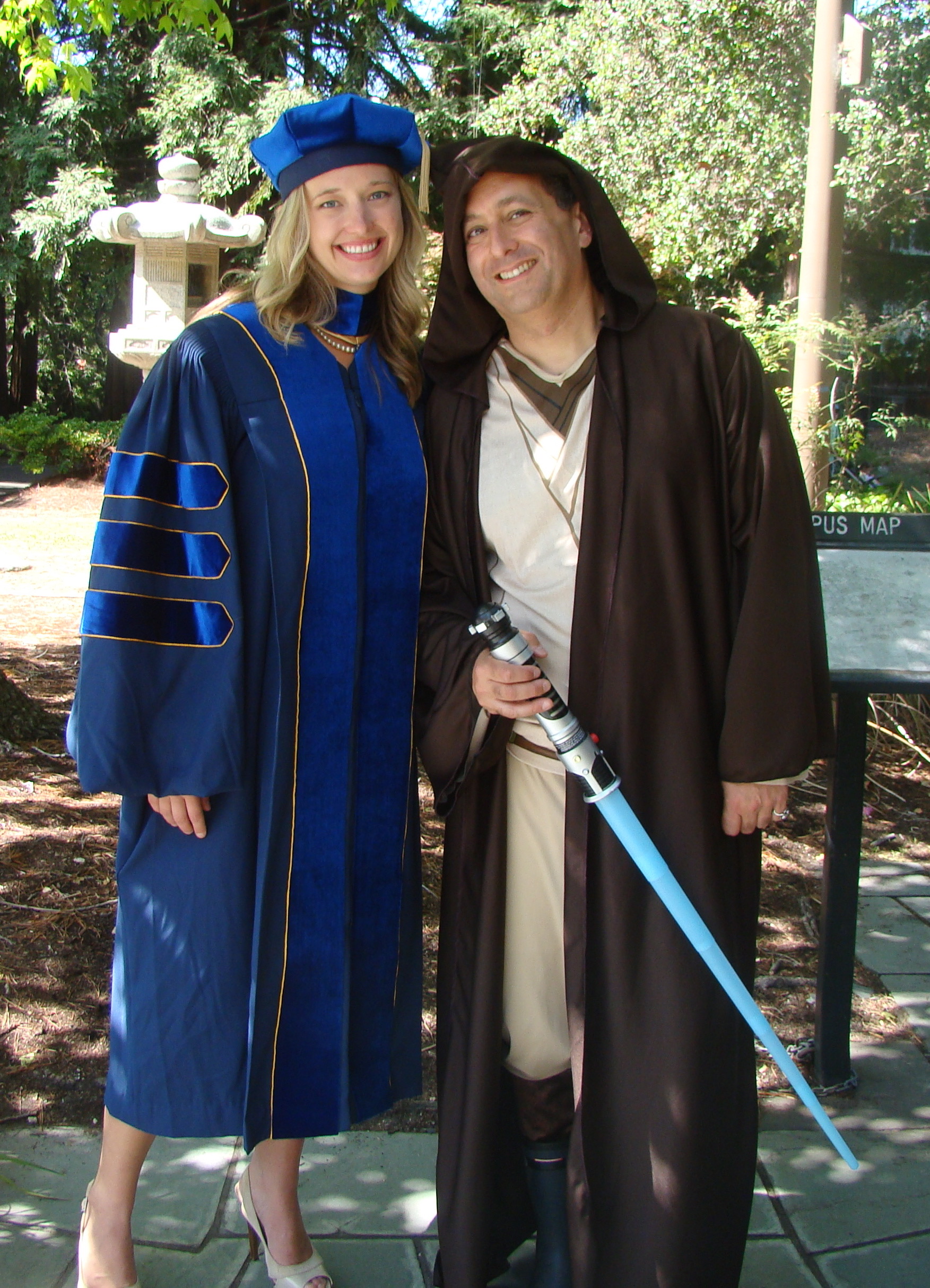 a woman in blue robes posing beside man in brown robe carrying light saber