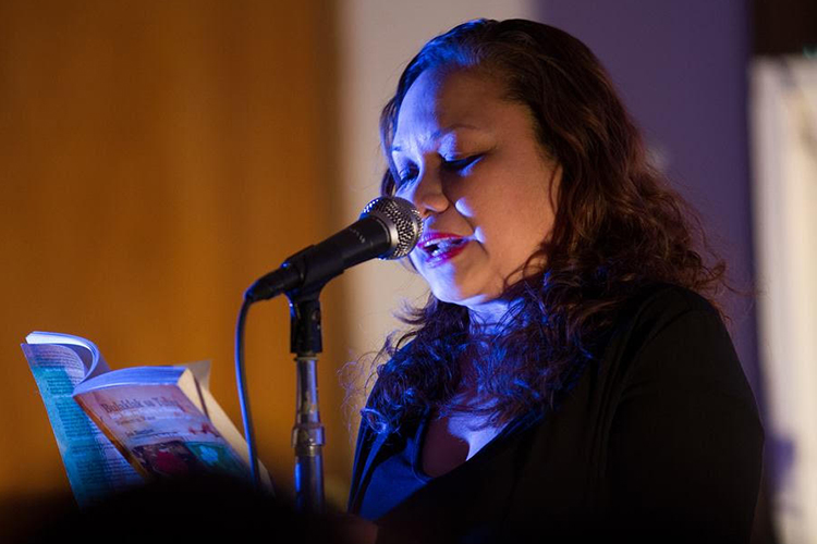 Joie Barrios-Leblanc reading a poem at a microphone.