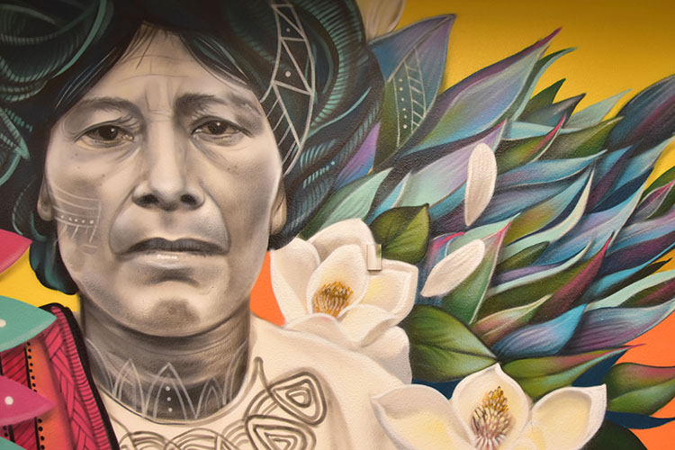 A mural of an elder Mexican women with colorful flowers in the background.
