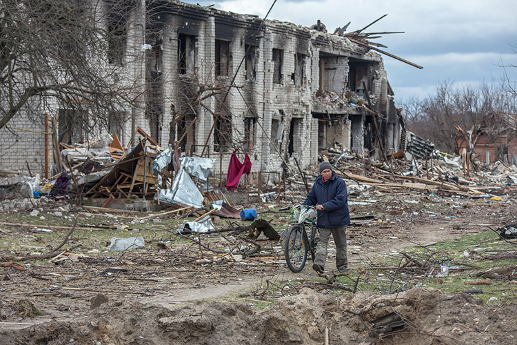 a person walks a bicycle by a destroyed building