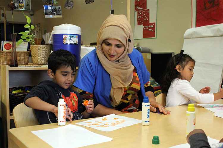 A female child care worker sits between two young children