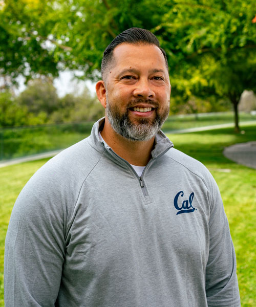 Graig Chow, director of high performance and well-ness for Cal Athletics' Cameron Institute for Student-Athlete Development looks at the camera in a grey pullover that says Cal