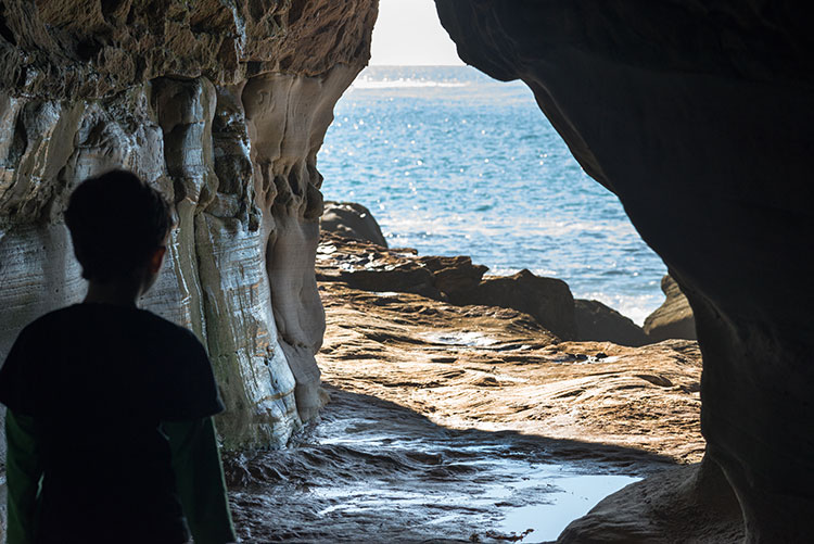 A child looking out from a cave at the ocean.