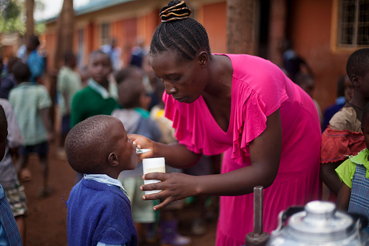 School worker gives a de-worming pill to a young student at a school in Western Kenya