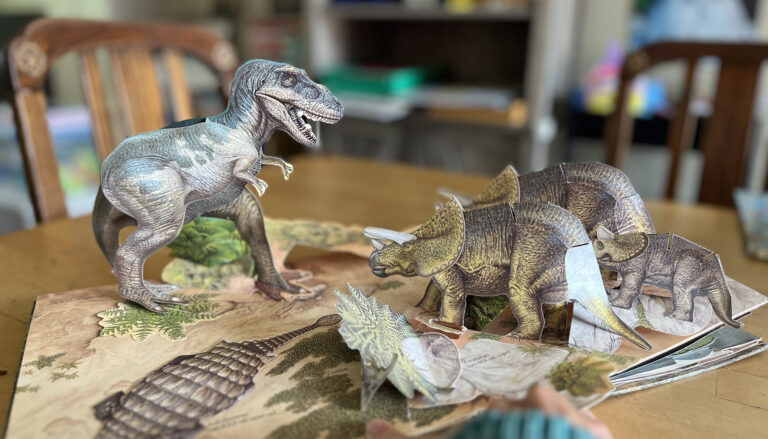 a page from a pop-up book shows a T. rex and other dinosaurs