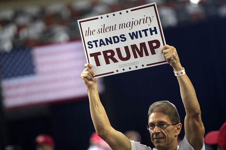 Lone man at campaign rally holds sign saying "the silent majority stands with Trump"