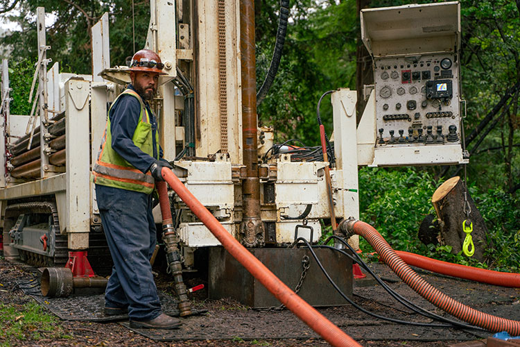 A photo shows a member of a drilling crew holding an orange pipe 