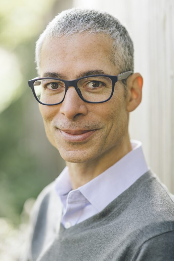 headshot of a man in glasses smiling